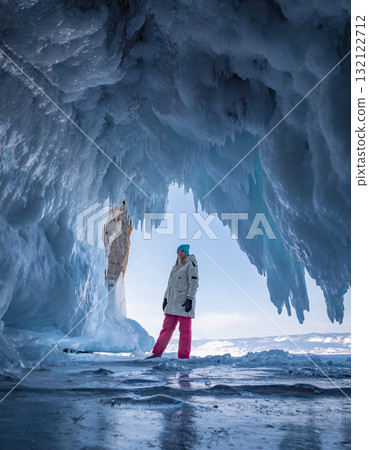 Young woman in winter gear stands inside a stunning ice cave on Baikal Lake. 132122712