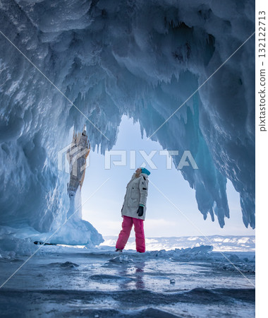 Young woman in winter gear stands inside a stunning ice cave on Baikal Lake. Young woman in winter gear stands inside a stunning ice cave on Baikal Lake. 132122713