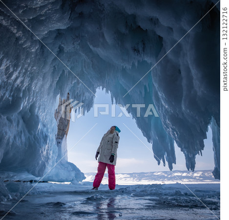 Young woman in winter gear stands inside a stunning ice cave on Baikal Lake. 132122716