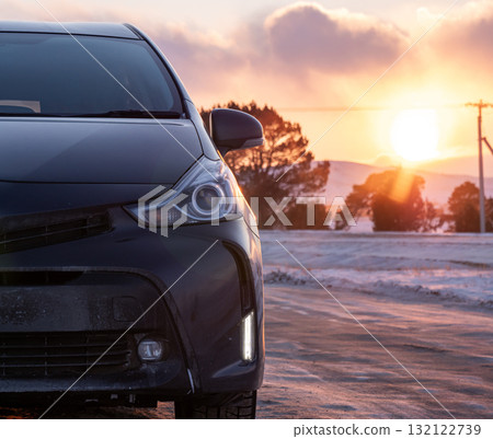 Black car parked on a snowy road during sunset near mountains reflecting golden light 132122739