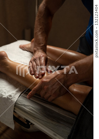 Close-up of a professional therapist giving a leg massage in a spa, applying oil and pressure with hands to relax muscles, improve circulation, and promote wellness in a calm environment. Close-up of a professional therapist giving a leg massage in a spa, applying oil and pressure with hands to relax muscles, improve circulation, and promote wellness in a calm environment. 132123404