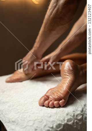 Close-up of a professional therapist performing a relaxing foot and leg massage in a spa, with oil on the skin, promoting wellness, relaxation, and circulation in a calm atmosphere. 132123407