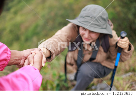 Two hikers on rocky mountain peak helping each other climb, symbol of teamwork, leadership, support, adventure, success, trust, exploration and outdoor lifestyle motivation in nature. Two hikers on rocky mountain peak helping each other climb, symbol of teamwork, leadership, support, adventure, success, trust, exploration and outdoor lifestyle motivation in nature. 132123633
