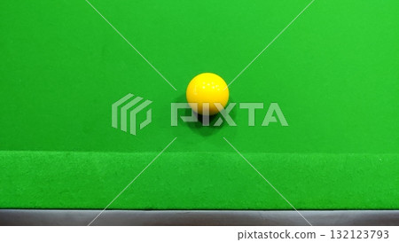 A yellow snooker ball resting on a green snooker table in a close up shot A yellow snooker ball resting on a green snooker table in a close up shot 132123793