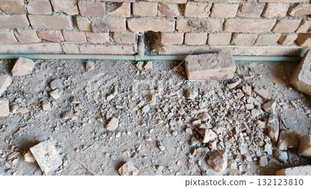 A damaged brick wall with a green pipe and rubble on the floor showing signs of construction work repair 132123810