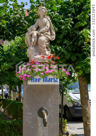 A religious statue of Virgin Mary with flowers and a water spout in front of the Church of Our Lady in historic old town of Bruges, Belgium 132123843