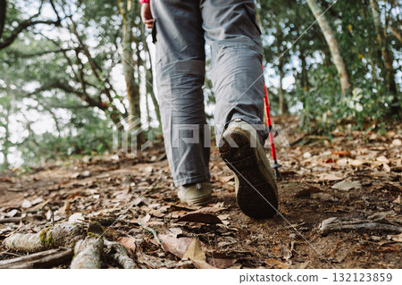 Close up of hiker walking uphill in forest with trekking pole, symbol of adventure, determination, outdoor lifestyle, hiking activity, travel journey and exploration in nature trail. 132123859