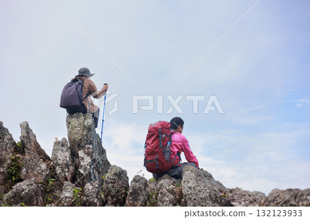 Two hikers with backpacks sitting on rocky mountain peak under blue sky, symbol of friendship, teamwork, freedom, inspiration, exploration, outdoor lifestyle and travel journey in nature. Two hikers with backpacks sitting on rocky mountain peak under blue sky, symbol of friendship, teamwork, freedom, inspiration, exploration, outdoor lifestyle and travel journey in nature. 132123933