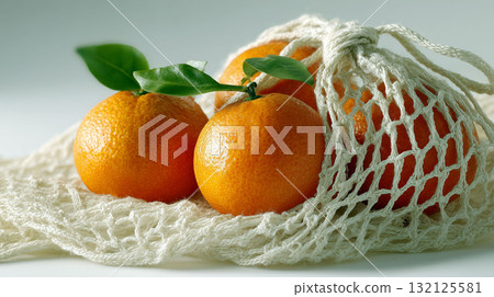 Fresh tangerines with green leaves in reusable cotton mesh bag on light background 132125581