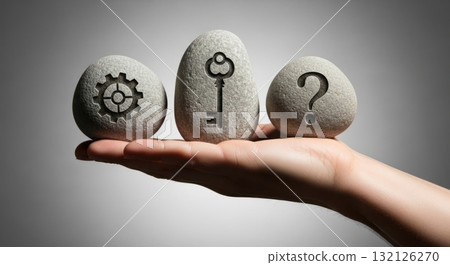 Human hand balancing three stones with symbols of gear, key, and question mark representing problem solving 132126270