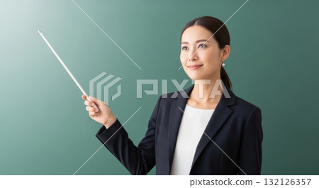 Smiling asian woman teacher in blazer holding a pointer stick against a green background 132126357