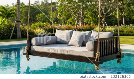 Luxurious wooden swing bed with grey cushions hanging over a swimming pool in a tropical garden Luxurious wooden swing bed with grey cushions hanging over a swimming pool in a tropical garden 132126365