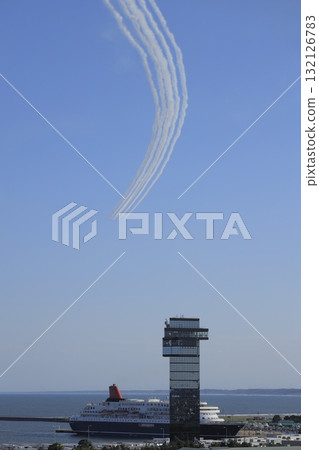 在晴朗的藍天背景下，藍色衝擊波飛機噴出濃煙，飛過茨城縣大洗町海洋塔和一艘大型客輪。 132126783