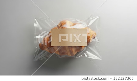 A single golden brown flaky croissant sealed in a clear plastic bag with a blank label 132127305