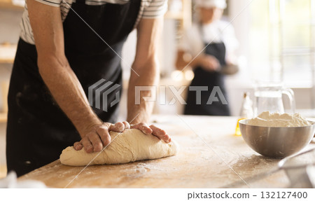 Closeup of baker hands kneading raw dough on kitchen table in bakery Closeup of baker hands kneading raw dough on kitchen table in bakery 132127400