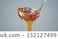 Glossy golden caramel sauce dripping from a metal ladle in thick viscous strands 132127499