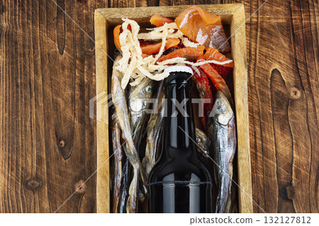 Beer and dried fish on wooden surface. 132127812
