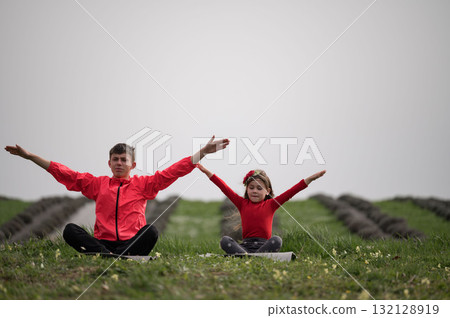 Two joyful children practicing yoga in a serene green field surrounded by rows of earth and budding flowers in the embrace of a cloudy morning sky 132128919