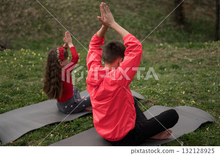Children practicing yoga outdoors, embracing nature's tranquility on a serene spring day, smiling and connecting, fostering mindfulness together in a beautiful landscape Children practicing yoga outdoors, embracing nature's tranquility on a serene spring day, smiling and connecting, fostering mindfulness together in a beautiful landscape 132128925