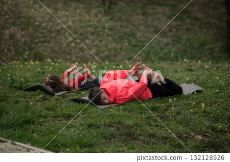 Practicing yoga outdoors with children enjoying relaxation and flexibility exercises on a grassy patch under a serene sky in early morning light 132128926