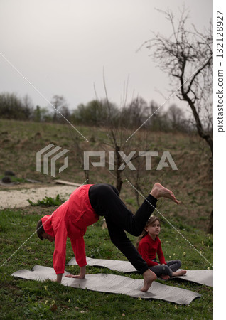 Sunset yoga practice in serene countryside with child observing a handstand on a mat, showcasing the bond between nature and mindful movement 132128927