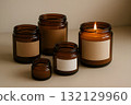 Minimal amber glass jars with blank labels, one lit candle, on a neutral beige background 132129960