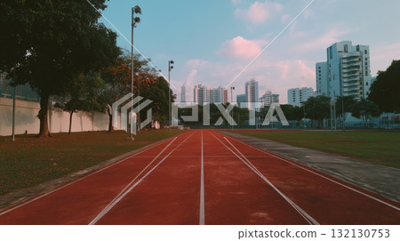 Red athletic track leading towards city skyline under a clear blue sky with scattered clouds 132130753