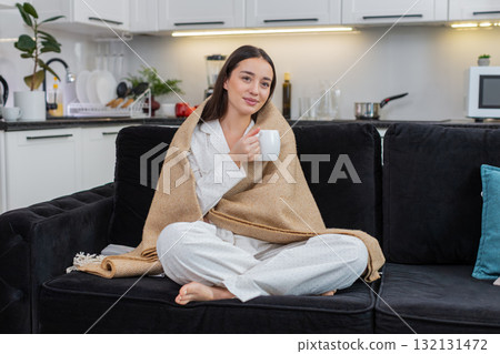 Young woman holds cup of tea wrapped in blanket relax calm cozy rest soft smile quiet evening hush Young woman holds cup of tea wrapped in blanket relax calm cozy rest soft smile quiet evening hush 132131472