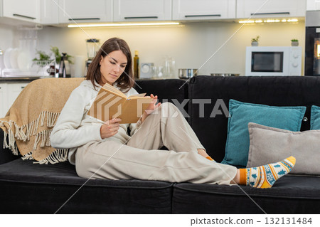 Young woman reads book enjoys leisure comfort quiet time smiles while turning pages with care slow Young woman reads book enjoys leisure comfort quiet time smiles while turning pages with care slow 132131484
