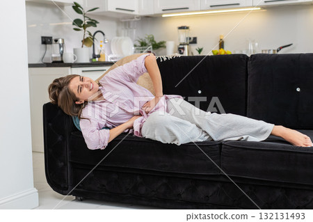 Young woman holds stomach with cramps after greasy foods or period pains rests and seeks for relief Young woman holds stomach with cramps after greasy foods or period pains rests and seeks for relief 132131493