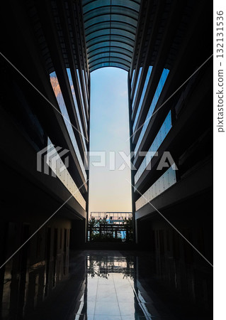 A Serene Perspective: The Tranquil Beauty of an Architectural Corridor Framed by Tall Buildings and a Glimpse of Nature Beyond at Dusk A Serene Perspective: The Tranquil Beauty of an Architectural Corridor Framed by Tall Buildings and a Glimpse of Nature Beyond at Dusk 132131536