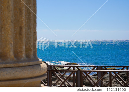 A Serene Coastal View Featuring Crystal-Clear Blue Waters, Rocky Shoreline, and Elegant Architectural Details in the Foreground 132131600