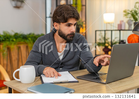 Indian man studies paper reports compares data with laptop focused look careful office work serious Indian man studies paper reports compares data with laptop focused look careful office work serious 132131641
