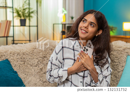Indian woman reads smartphone message smiles holds phone to chest moved by touching text feeling joy Indian woman reads smartphone message smiles holds phone to chest moved by touching text feeling joy 132131732