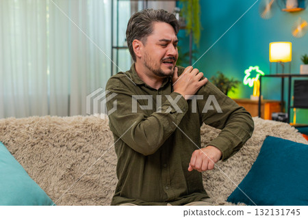 Middle-aged man gripping sore shoulder grimaces pain injury discomfort muscle strain seeking relief 132131745