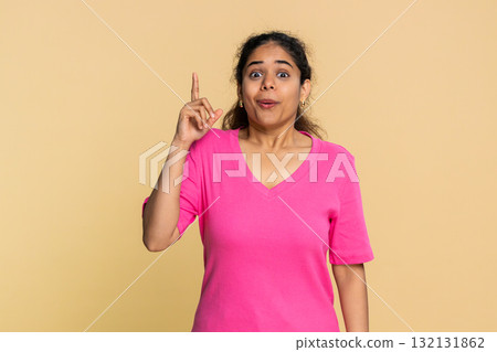 Indian woman smiling thoughtfully pointing up with finger creative idea isolated on beige background 132131862
