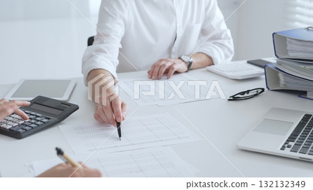 Professional women collaborating, reviewing financial reports using calculator, laptop, discussing workplace strategy with team. Audit and taxes in business 132132349