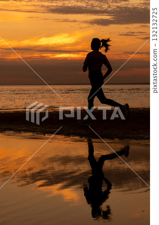 Silhouette of woman doing sports by the sea during an amazing sunset, jogging. 132132725