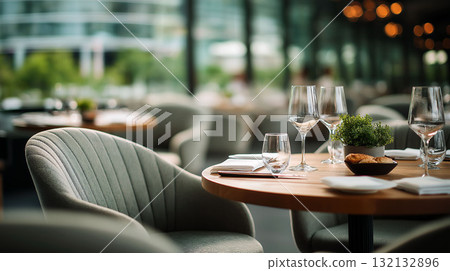 Elegant modern restaurant table setting with wine glasses, napkins and green plant in soft natural light 132132896