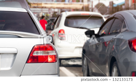 Rear side view of silver car with turn on brake light. Trffic jam on the aspahlt road in the day time. Many cars in the city in business time. 132133173