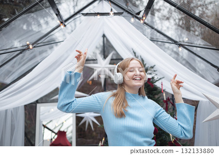 Happy blonde Caucasian woman enjoying music in headphones in festive Christmas interior 132133880