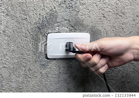 a hand pulling the plug out of an outlet 132133944