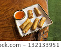 Deep fried Filipino pork lumpia spring roll with dipping sauce on a plate on a natural wooden table 132133951