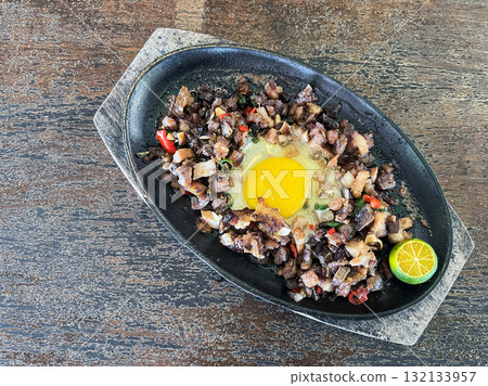 Sizzling pork sisig, a Filipino skillet dish served on a wooden tray with calamansi 132133957