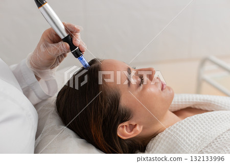 Trichologist doing woman hair regeneration procedure, dermapen microneedling, vitamin injections Trichologist doing woman hair regeneration procedure, dermapen microneedling, vitamin injections 132133996