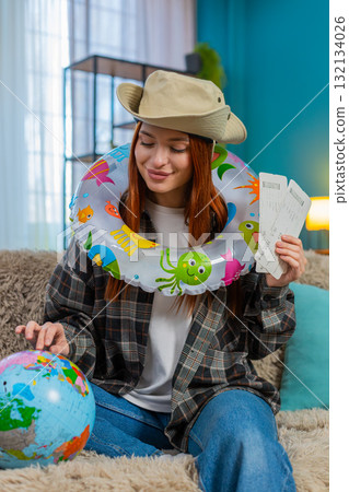 Young woman on sofa with swim ring holding globe and plane tickets planning exciting future trip Young woman on sofa with swim ring holding globe and plane tickets planning exciting future trip 132134026