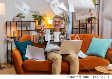 Stressed man freelancer reviewing business charts and graphs and throwing papers unpaid bills in air Stressed man freelancer reviewing business charts and graphs and throwing papers unpaid bills in air 132134101
