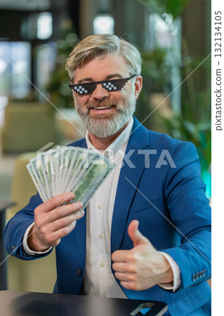 Rich mature businessman putting on thug life sunglasses showing money dollar in modern office lobby Rich mature businessman putting on thug life sunglasses showing money dollar in modern office lobby 132134105