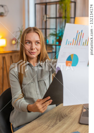 Happy mature businesswoman freelancer analyzing graph documents sitting at home office table desk 132134174