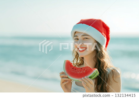 Smiling young woman in a Santa hat holding a slice of watermelon on the beach under bright sunlight Smiling young woman in a Santa hat holding a slice of watermelon on the beach under bright sunlight 132134415
